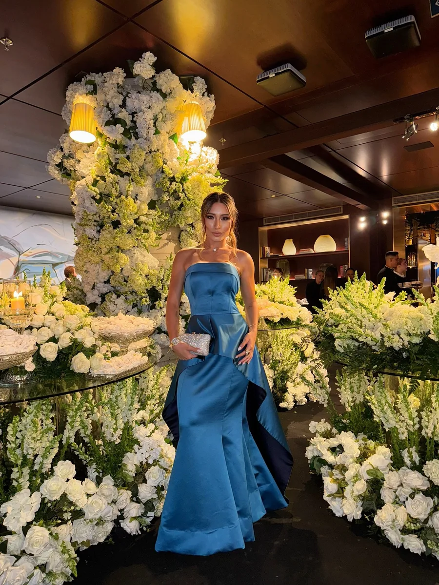 Rapha Alvez de vestido azul de cetim em evento decorado com flores brancas