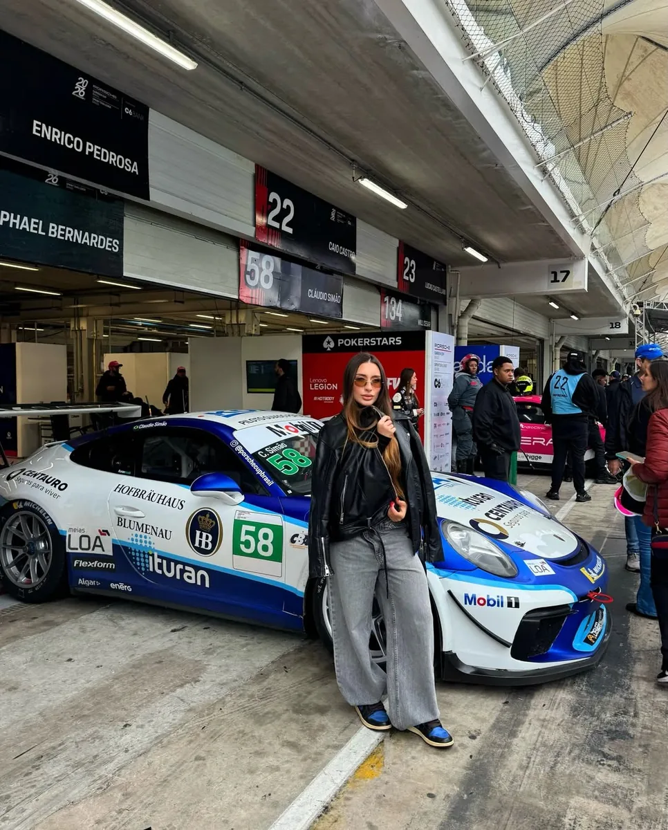 Rapha Alvez ao lado de um carro de corrida no paddock de uma prova de automobilismo