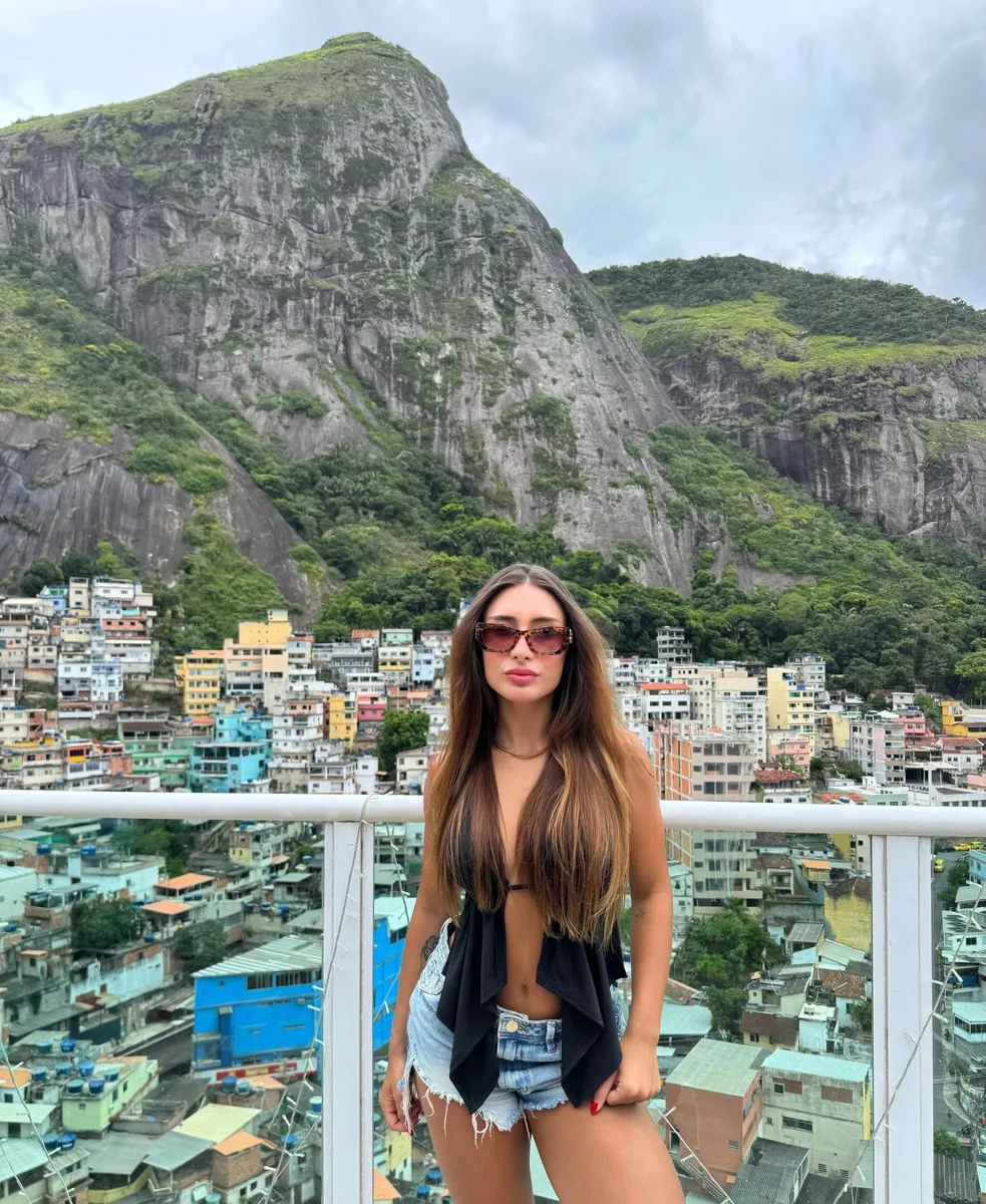 Rapha Alvez em varanda com vista para as montanhas e casas do Rio de Janeiro